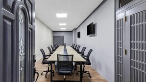 Uma sala de conferências com uma mesa comprida, cadeiras pretas e piso de madeira.