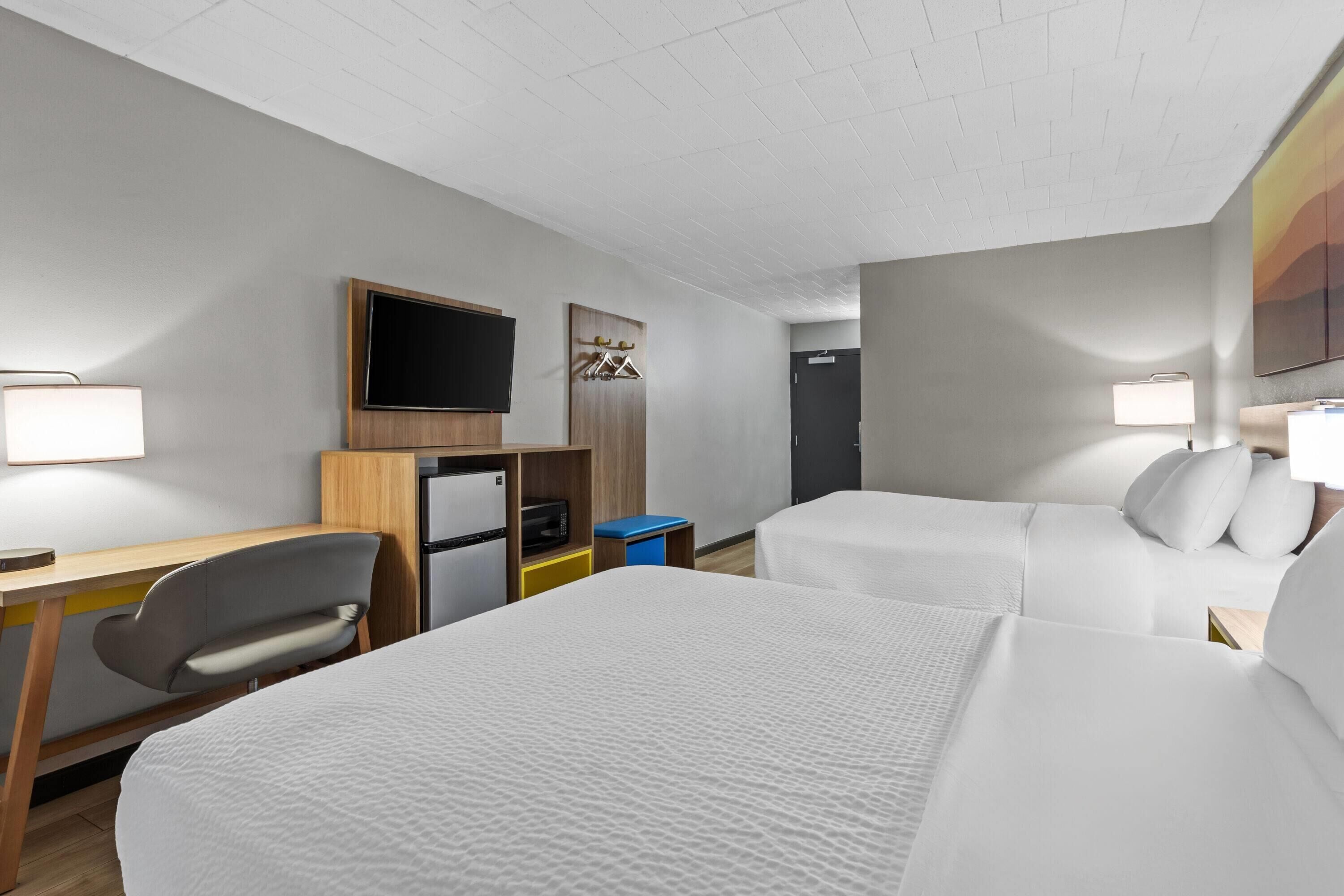 Een hotelkamer met twee bedden, een bureau, een stoel, een televisie en een kledingkast.