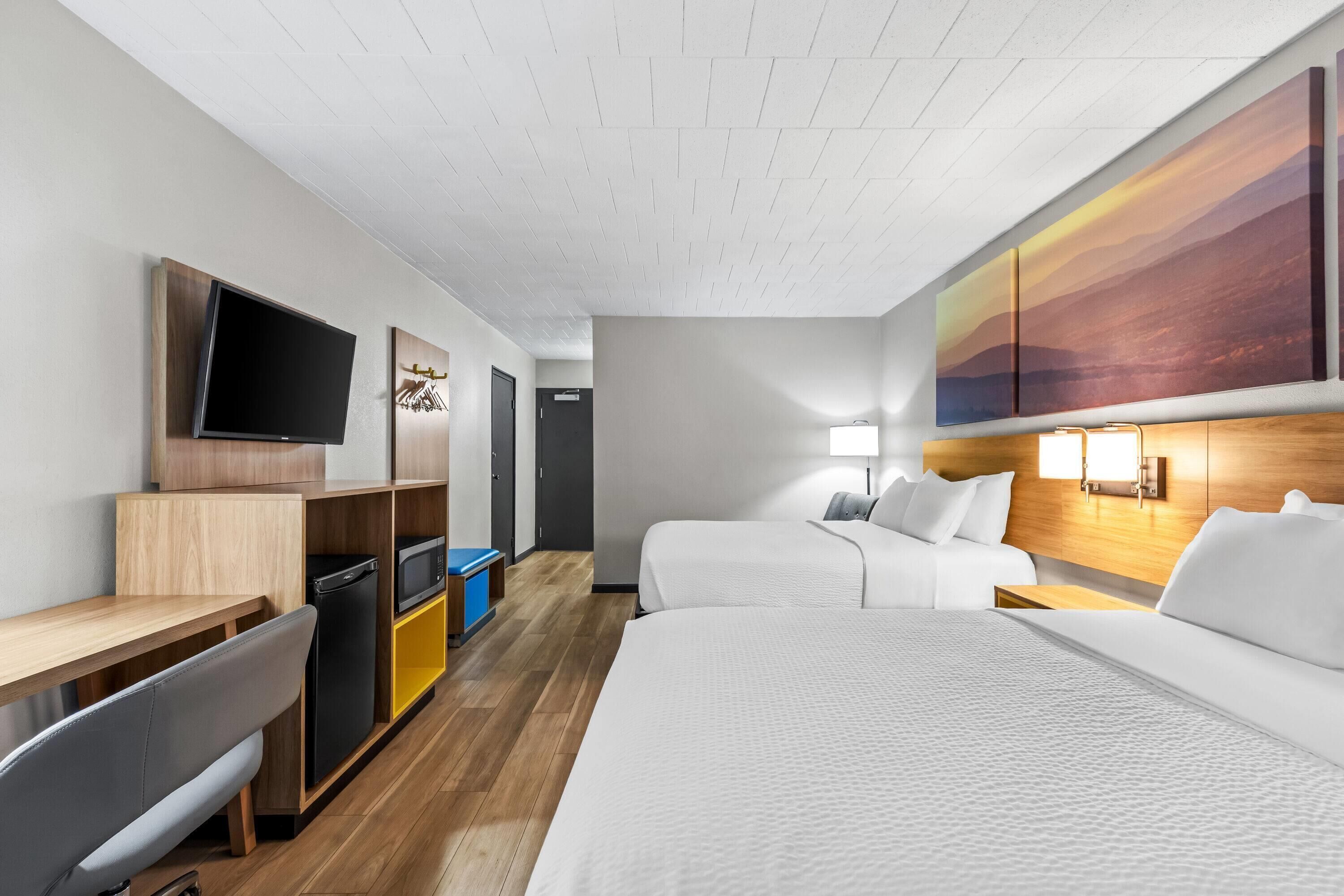 Habitación de hotel con cama, escritorio, televisor, microondas y armario.