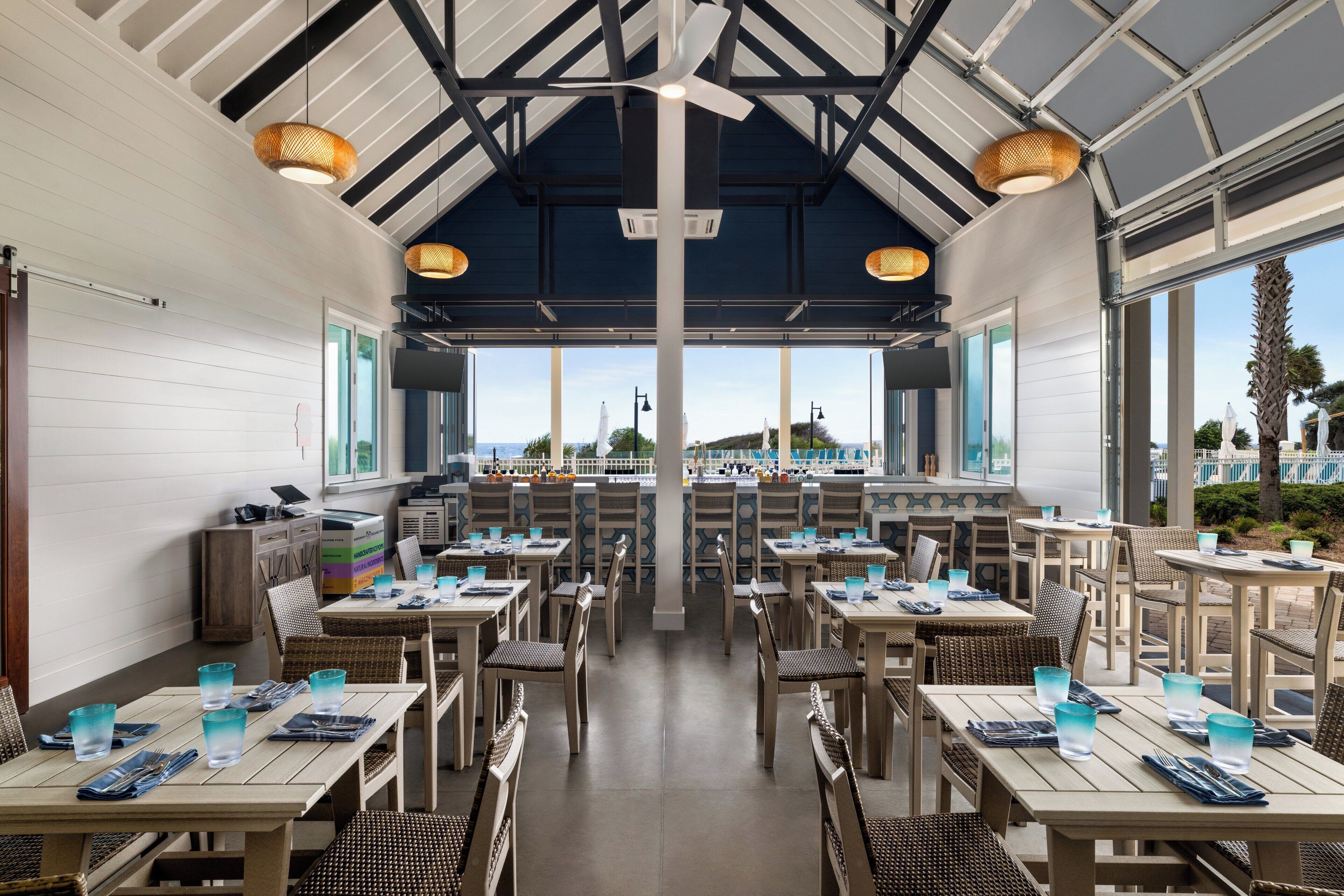 Un restaurant doté de nombreuses tables et chaises, d’un ventilateur de plafond et de grandes fenêtres donnant sur l’extérieur.