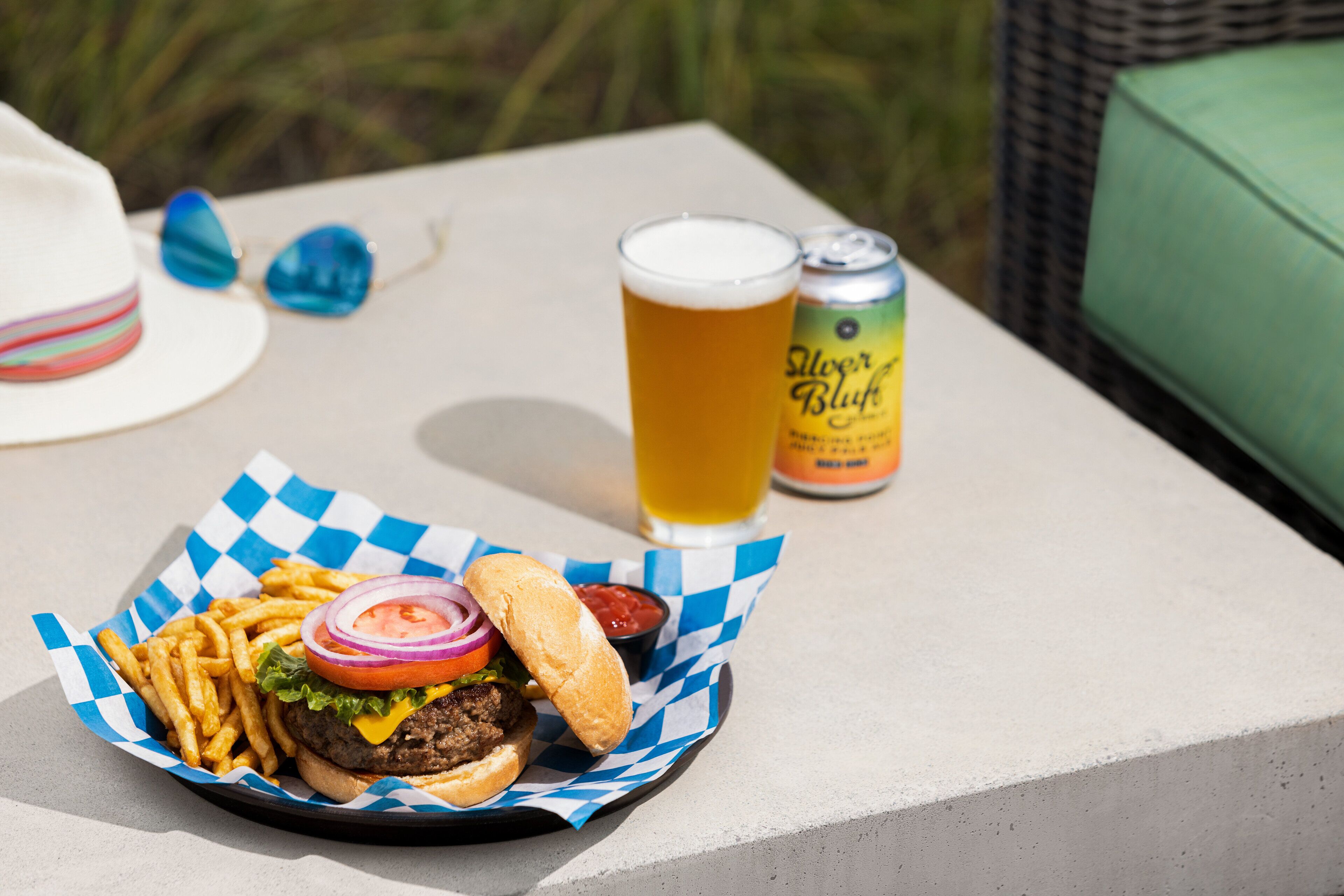 A meal consisting of a burger, fries, and a drink on a table outdoors.