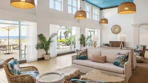 A spacious living area with a large sofa, wicker chairs, and a round table. There are large windows and doors leading to an outdoor patio with a view of the ocean. - Holiday Inn Resort Jekyll Island by IHG (Jekyll Island)