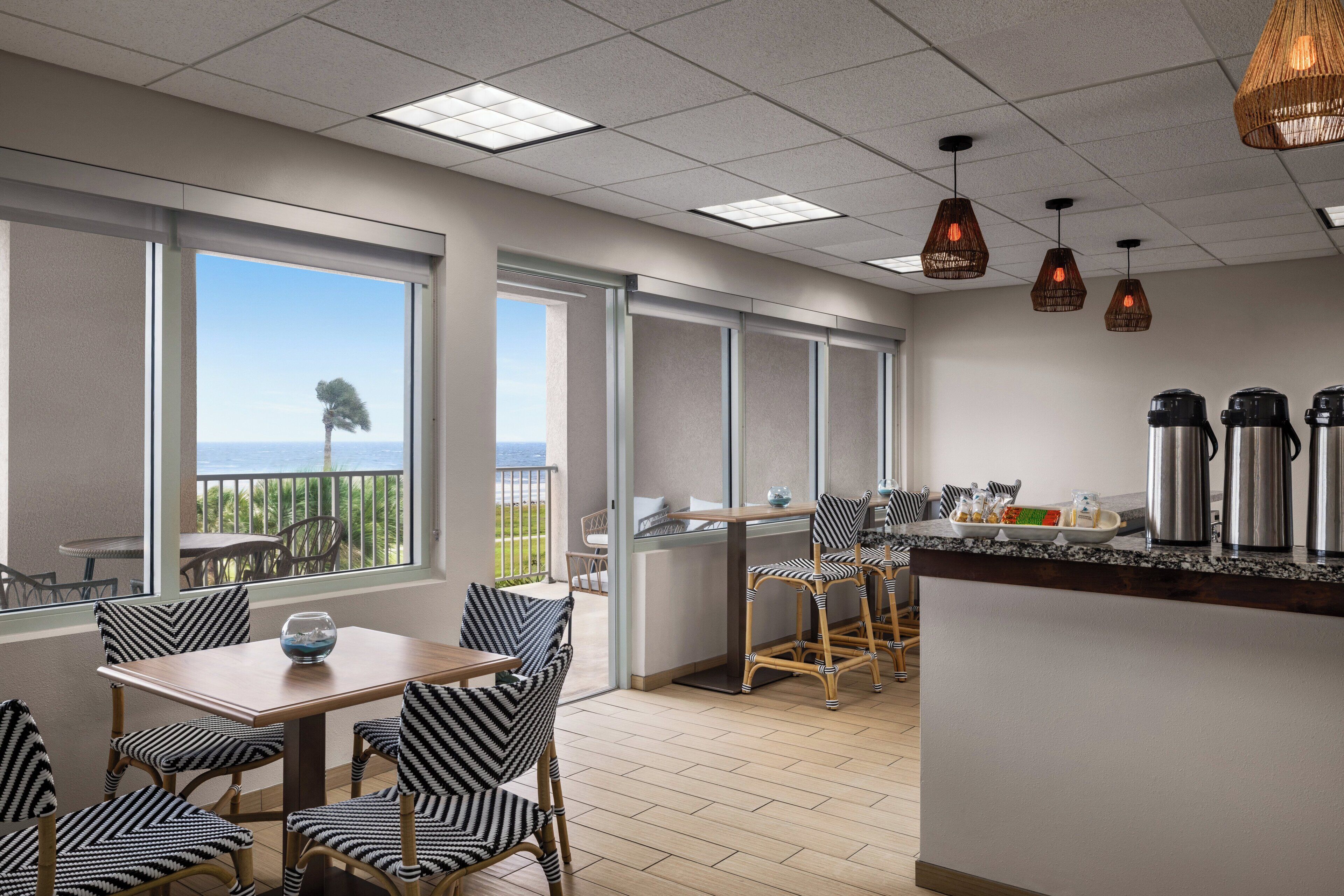 A modern kitchen with a bar area, large windows with a view, and a dining area with striped chairs.