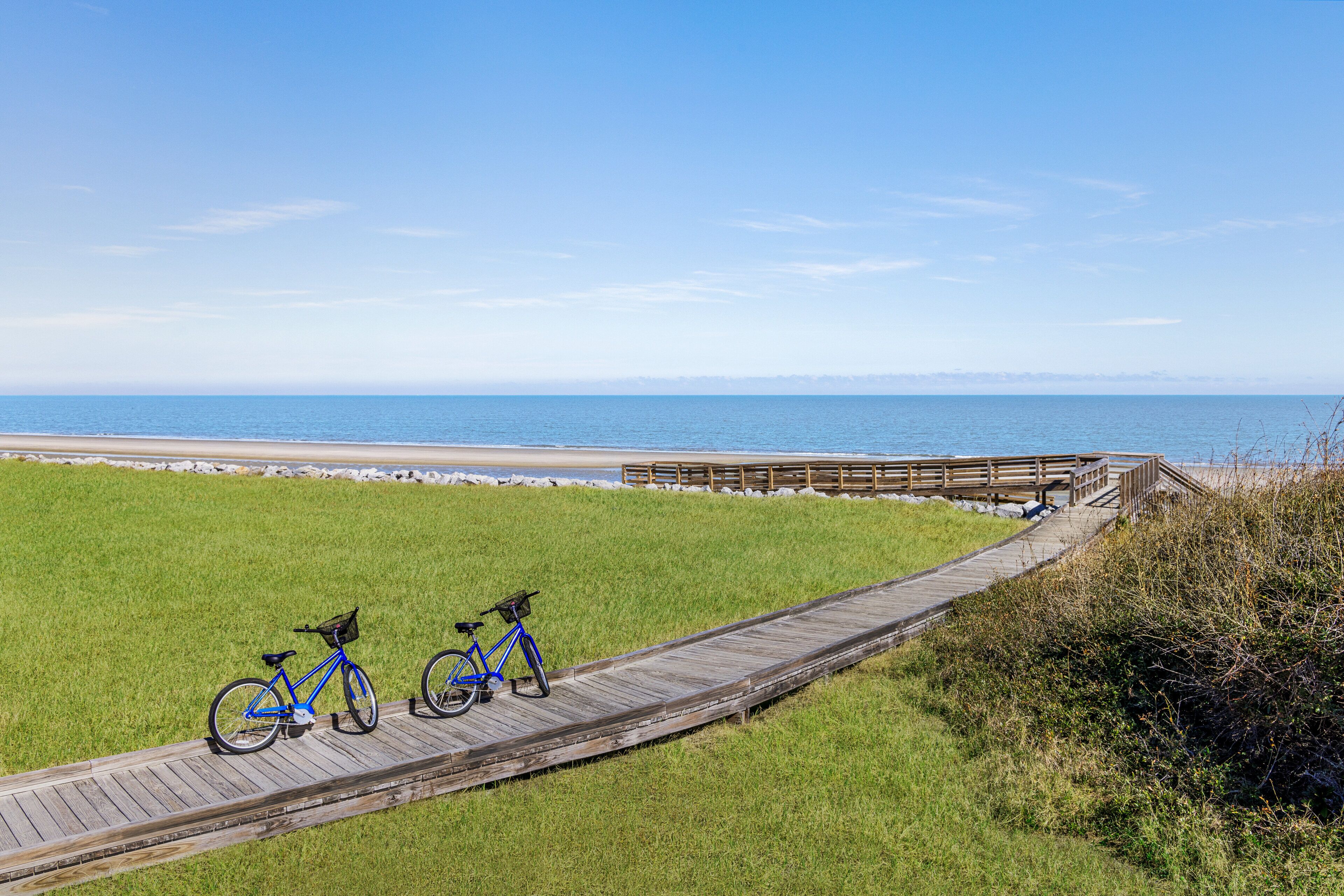 A wooden boardwalk leading to a beach with two bicycles parked on it.