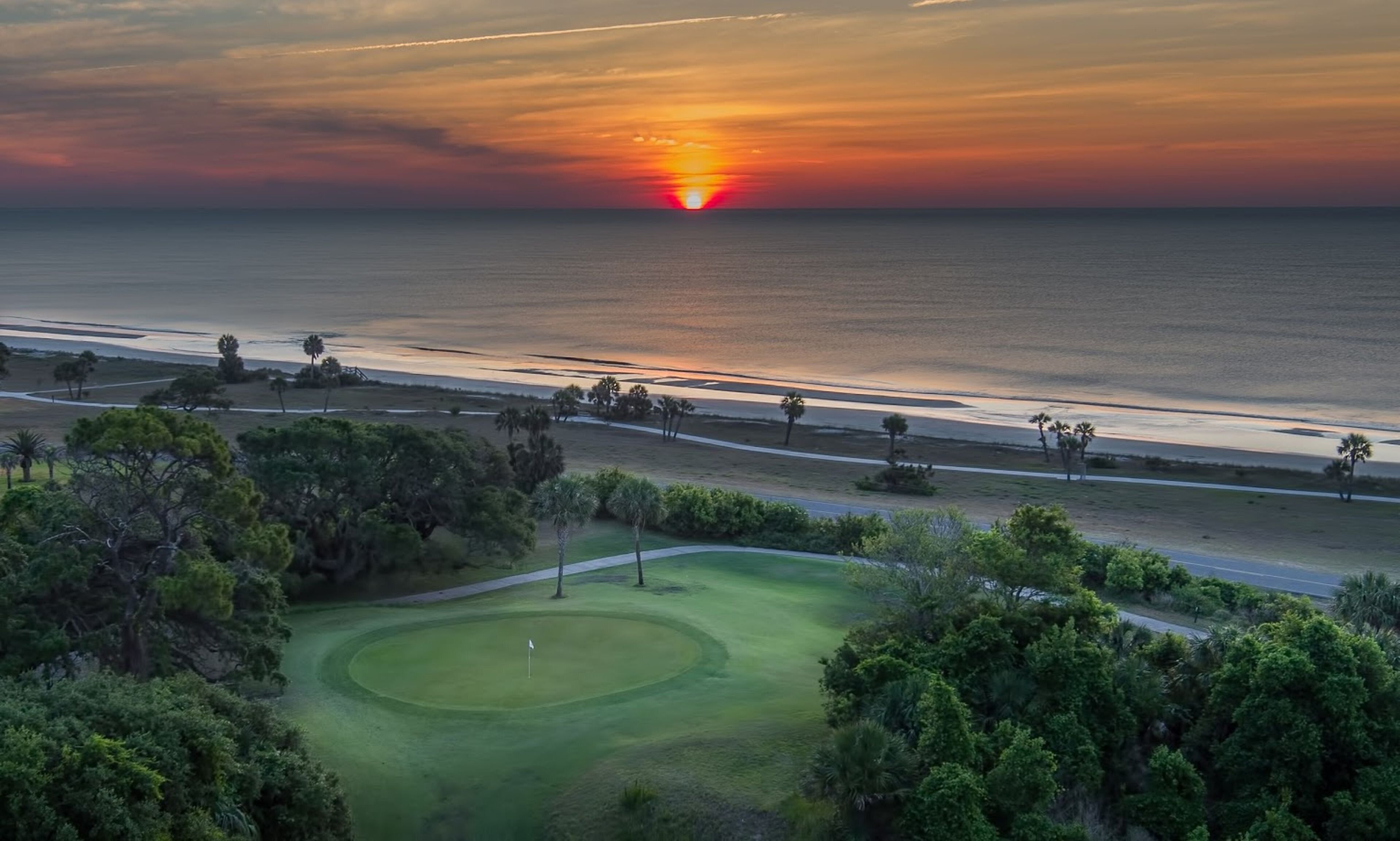 Campo de golf con vista al océano y al atardecer.