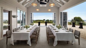 A dining area with two long tables set for a meal, large windows, and a view of the outdoors.