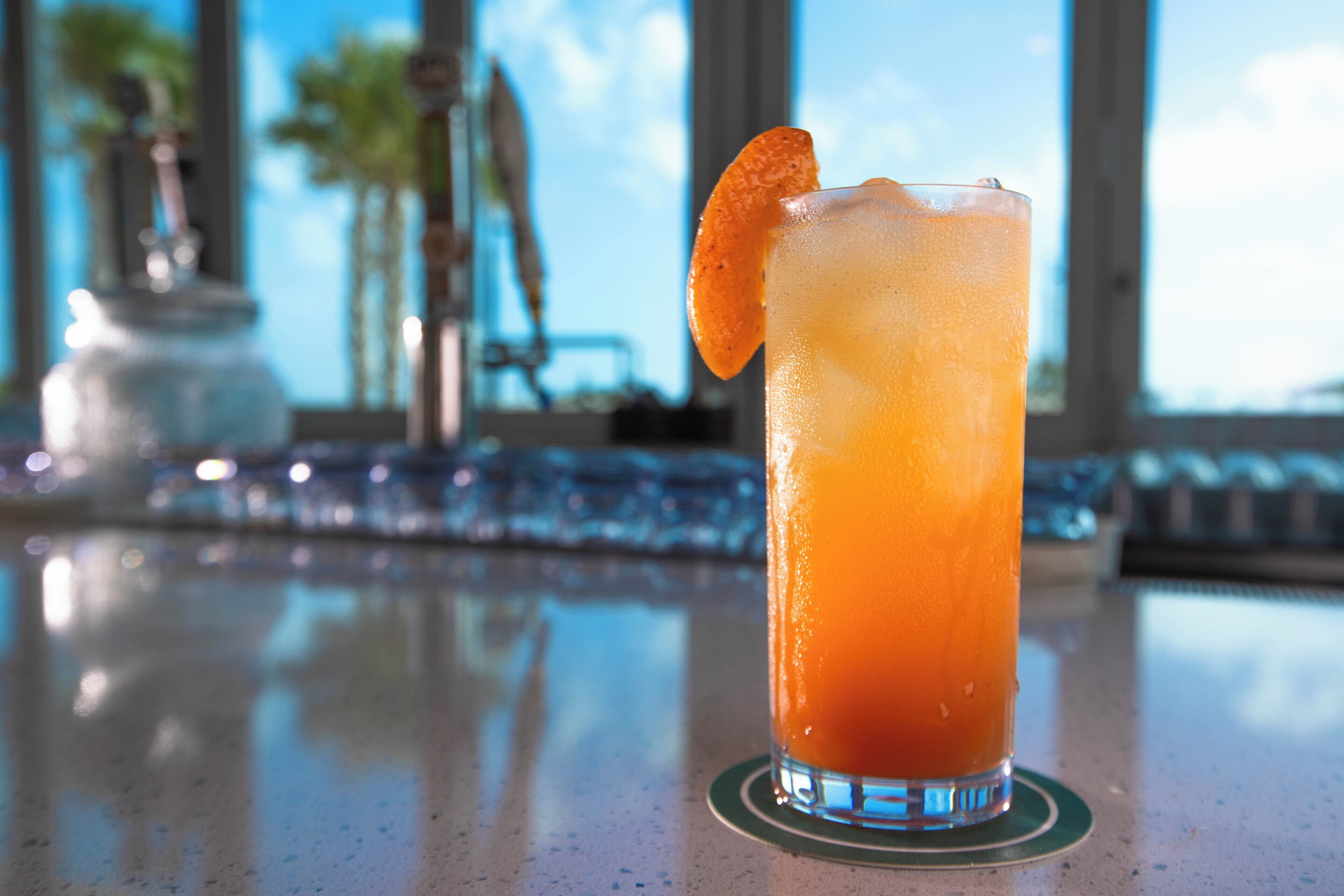 A tall glass with a citrus garnish on a bar counter.