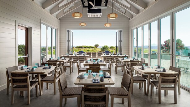 A spacious dining area with multiple tables and chairs, large windows offering a view of the outdoors, and a ceiling fan. - Holiday Inn Resort Jekyll Island by IHG (Jekyll Island)
