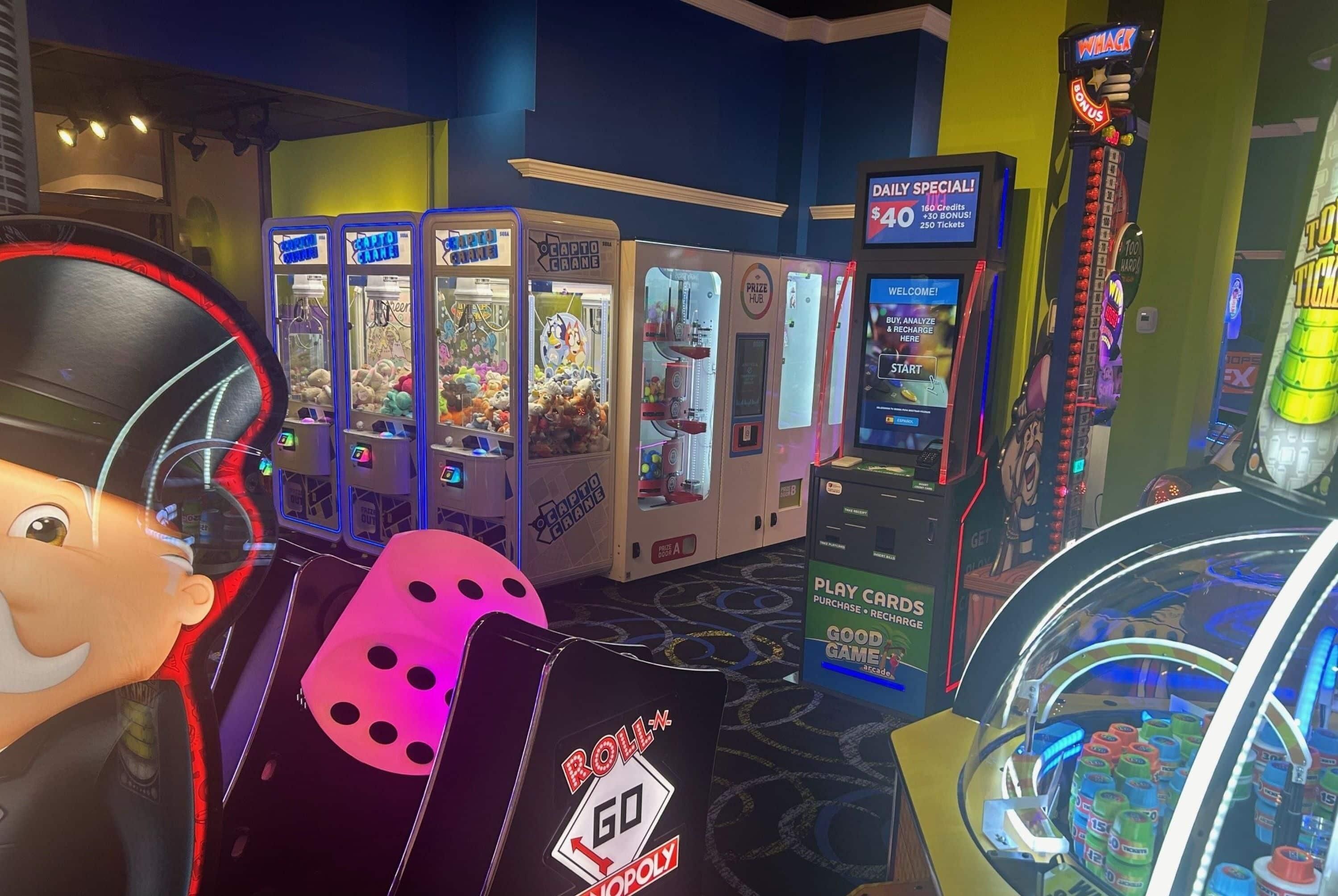 Una habitación con una máquina recreativa grande y colorida, un juego de mesa Go Monopoly y una máquina de pinzas.