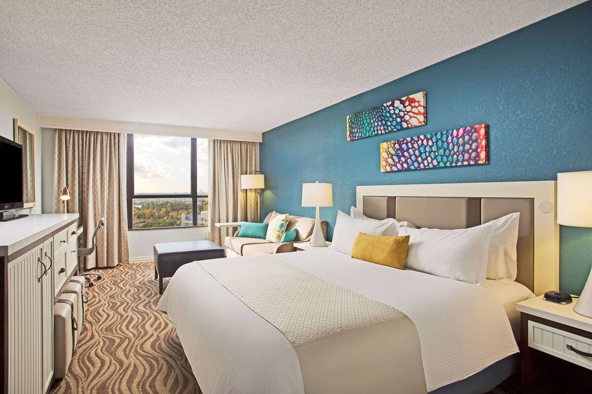Ein Hotelzimmer mit einem großen Bett, einem Schreibtisch, einem Fernseher und Blick auf die Stadt.