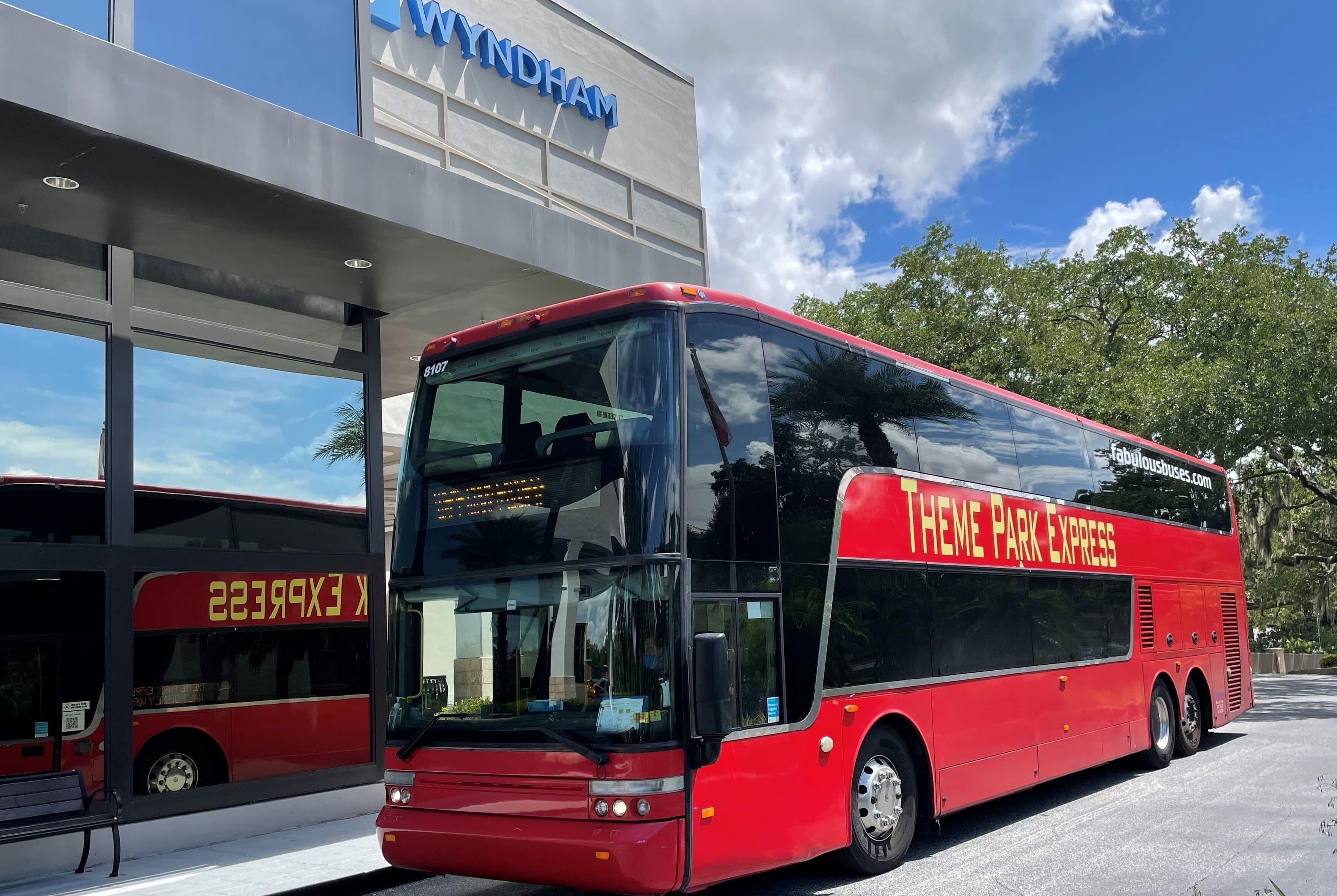 A red double-decker bus labeled 'THEME PARK EXPRESS' parked at a bus station with a building in the background.