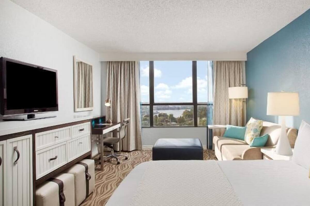 Ein Hotelzimmer mit Bett, Schreibtisch, Fernseher, Blick ins Freie und einem Vorhangfenster.