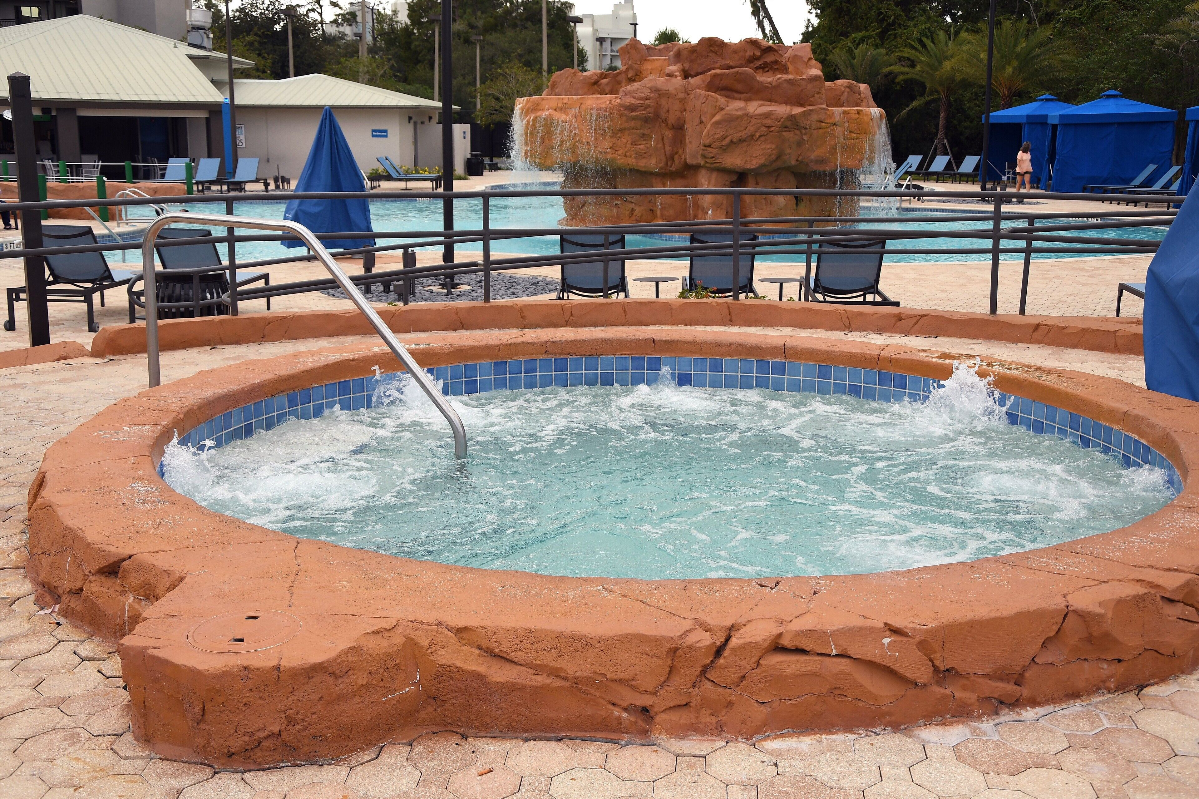 Un jacuzzi rodeado por una piscina con sillas de descanso y sombrillas.