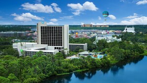 A modern hotel with a large glass facade, a swimming pool, and a view of a river and cityscape. - Wyndham Lake Buena Vista – Disney Springs® Area (Lake Buena Vista)