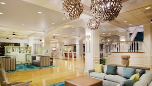 A spacious lobby with a wooden floor, a grey sofa set, a brown ottoman, and a staircase with a wooden railing. - Wyndham Lake Buena Vista – Disney Springs® Area (Lake Buena Vista)