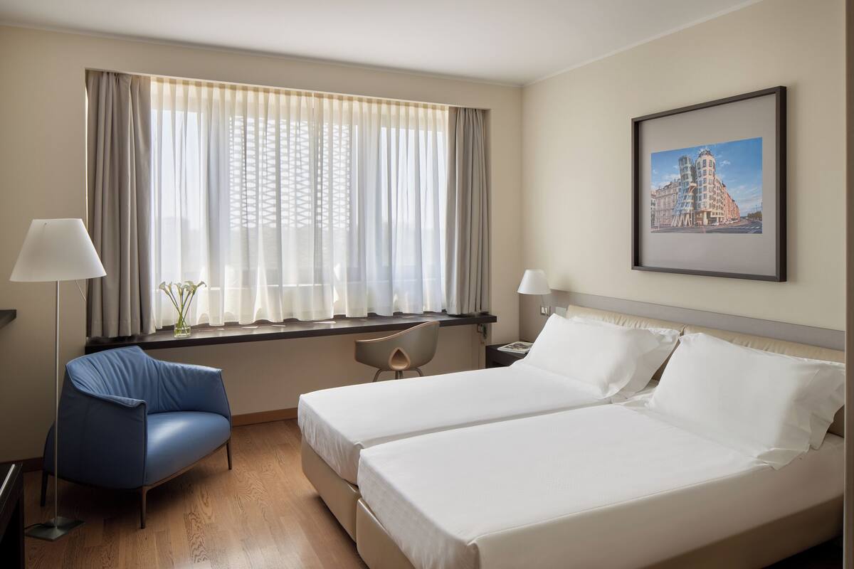 A hotel room with two beds, a desk, a chair, and a window with curtains.