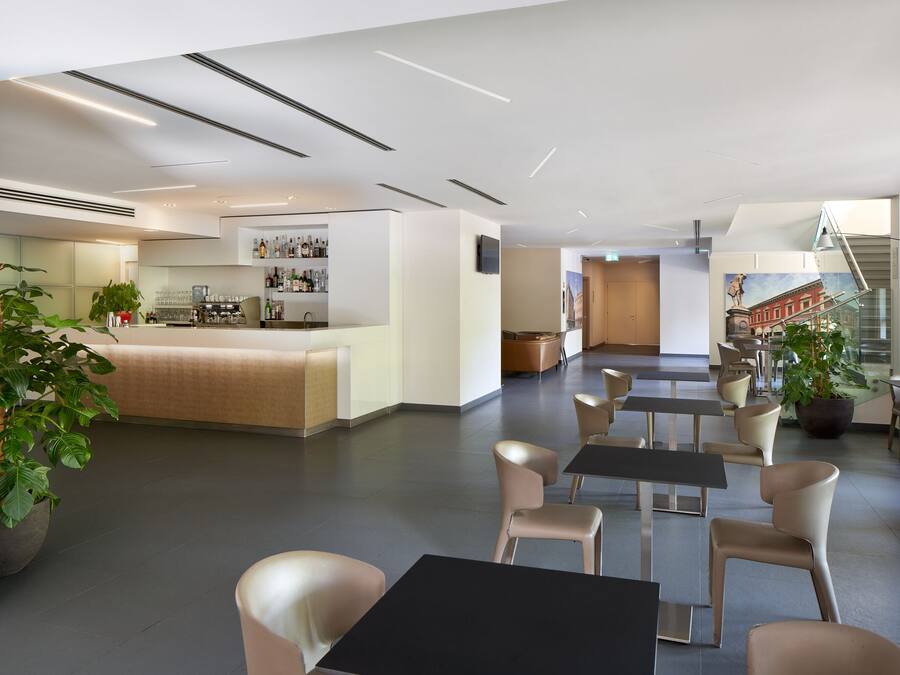 Un moderno vestíbulo de hotel con una zona de bar, disposición de asientos y una escalera que conduce a otro piso.