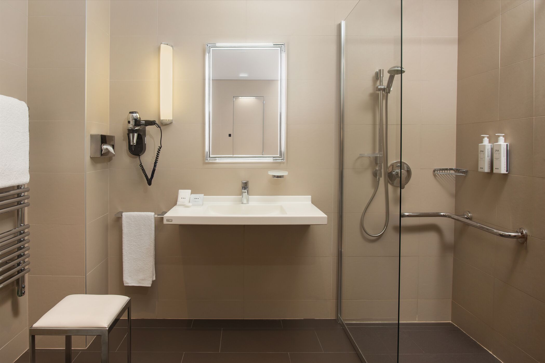Une salle de bain moderne avec une douche à l’italienne en verre, un lavabo blanc et un petit banc.