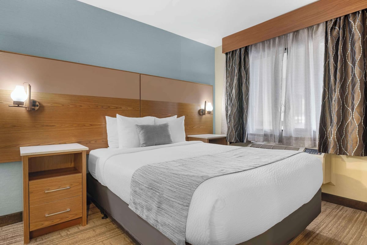 A hotel room with a large bed, wooden headboard, bedside tables, and a window with curtains.