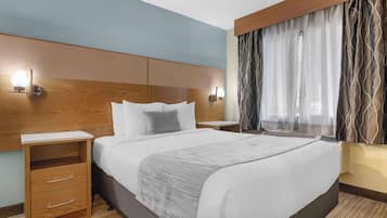 Une chambre d’hôtel avec un grand lit, une tête de lit en bois, des tables de chevet et une fenêtre avec des rideaux.