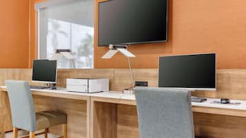 Un espacio de oficina moderno con dos escritorios, cada uno con monitor, teclado y ratón. Hay dos sillas, una en cada escritorio. Una impresora está en el escritorio de la izquierda. La habitación tiene paredes de madera y una ventana con persianas.