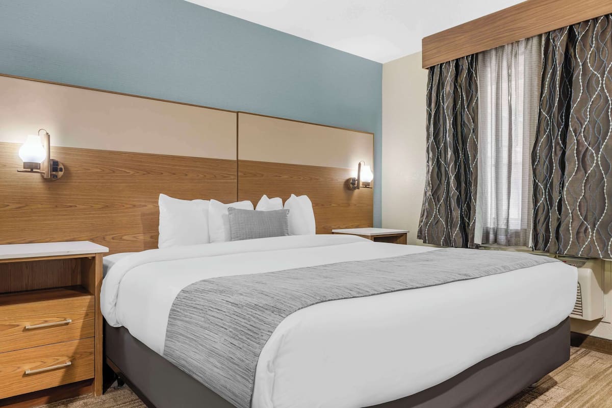 A hotel room with a large bed, wooden headboard, bedside tables, and a window with patterned curtains.