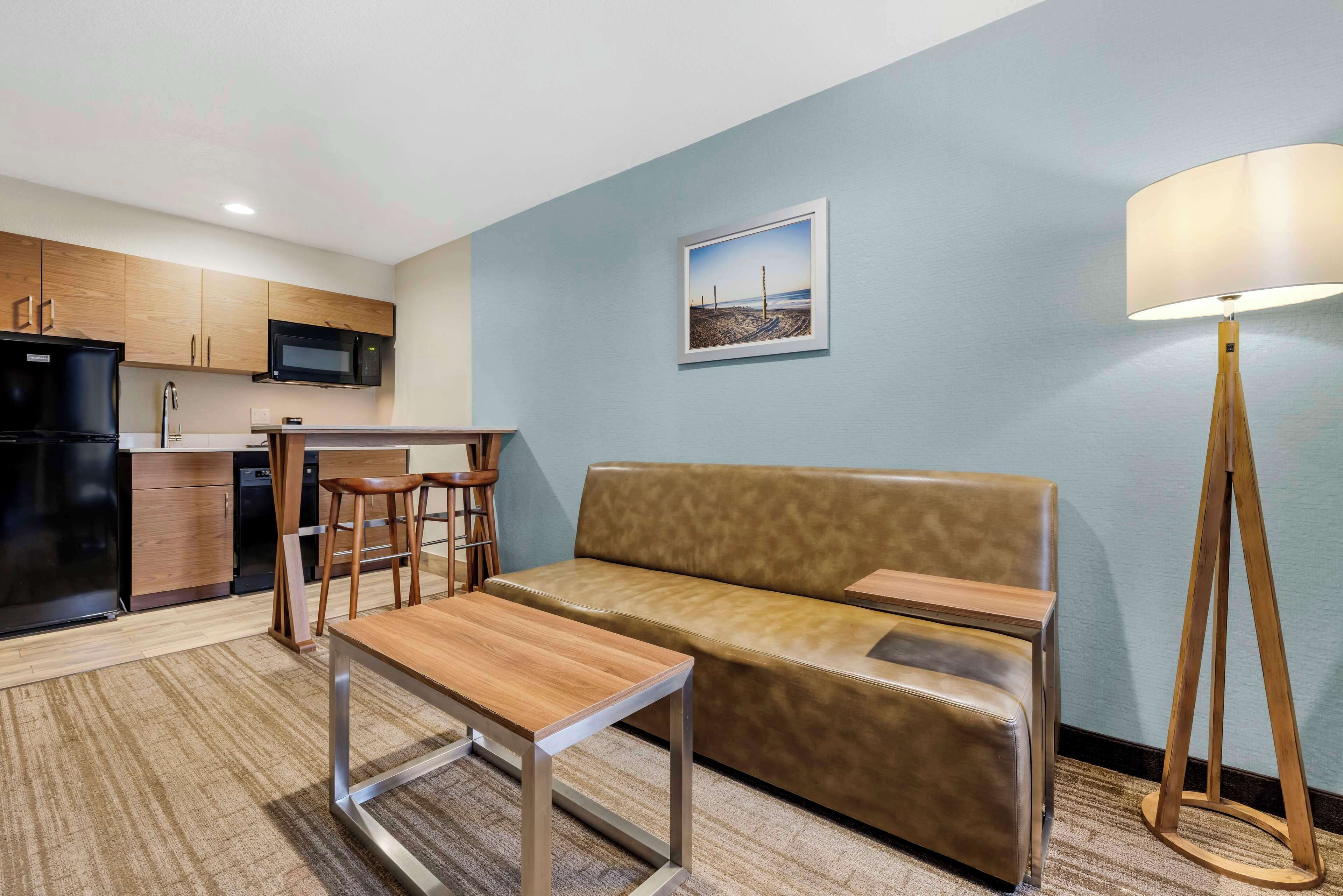 A compact living space with a kitchenette, a sofa, a small table, and a lamp.