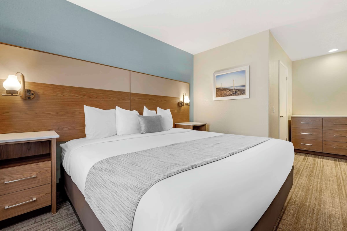 A hotel room with a large bed, wooden headboard, bedside tables, and a nightstand with a lamp.