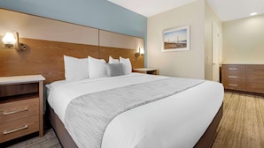 A hotel room with a large bed, wooden headboard, bedside tables, and a nightstand with a lamp.