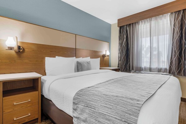 Habitación de hotel con una cama grande, cabecera de madera, mesitas de noche con lámparas y una ventana con cortinas estampadas.