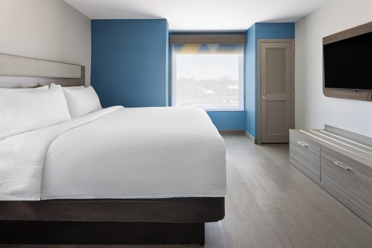 A modern hotel room with a large bed, a wardrobe, a television, and a window with a view.