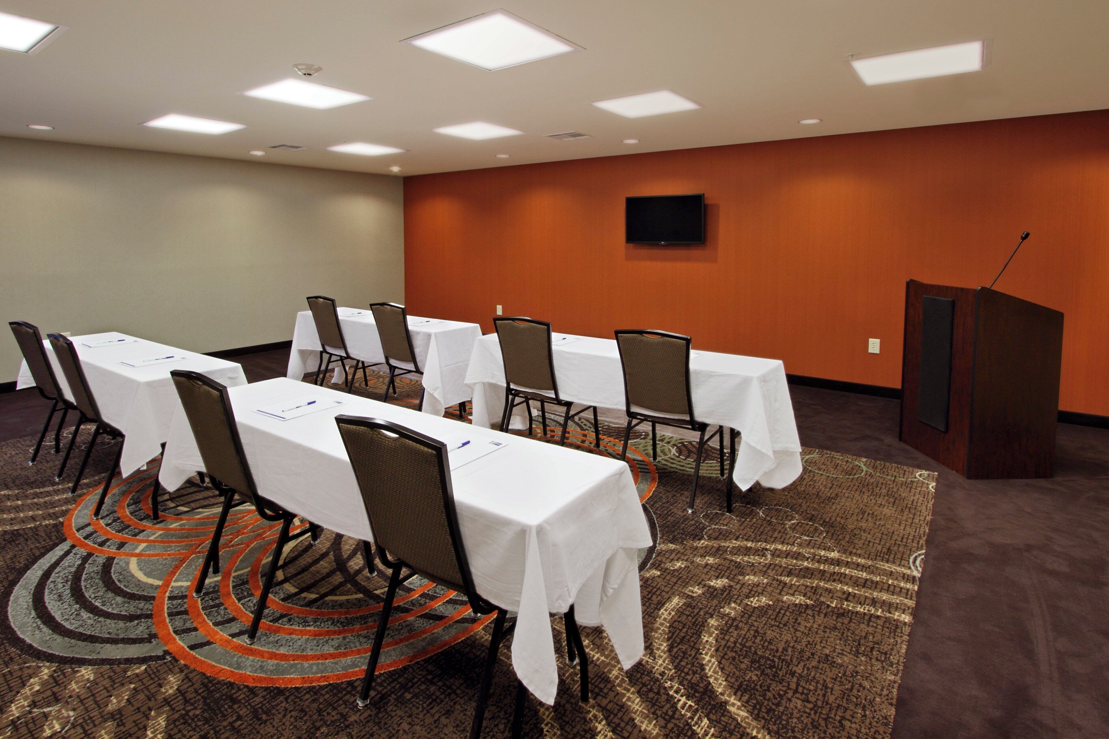 A conference room with tables and chairs, a podium, and a carpeted floor.
