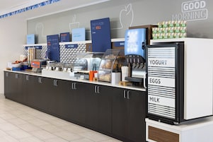 A breakfast station with labeled dispensers for yogurt, eggs, and milk, and various food items displayed on the counter.
