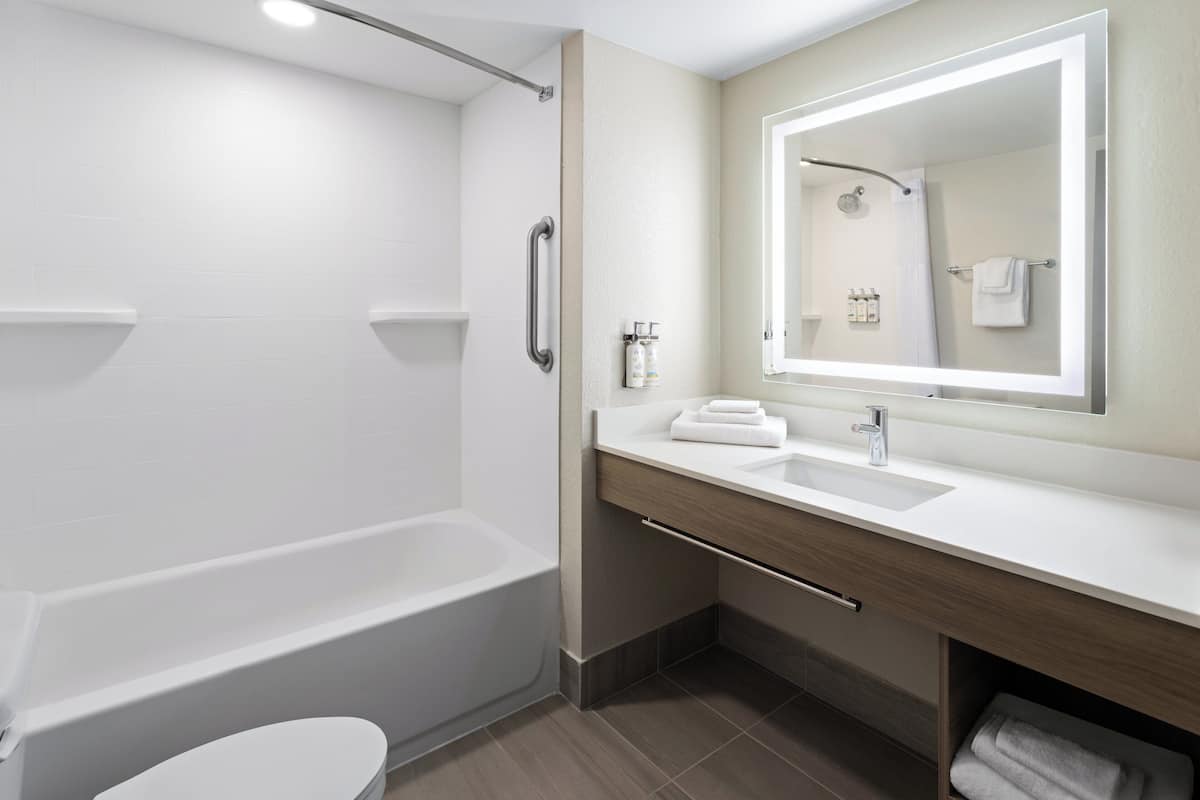 A modern bathroom with a bathtub, toilet, vanity with a mirror, and a towel rack.