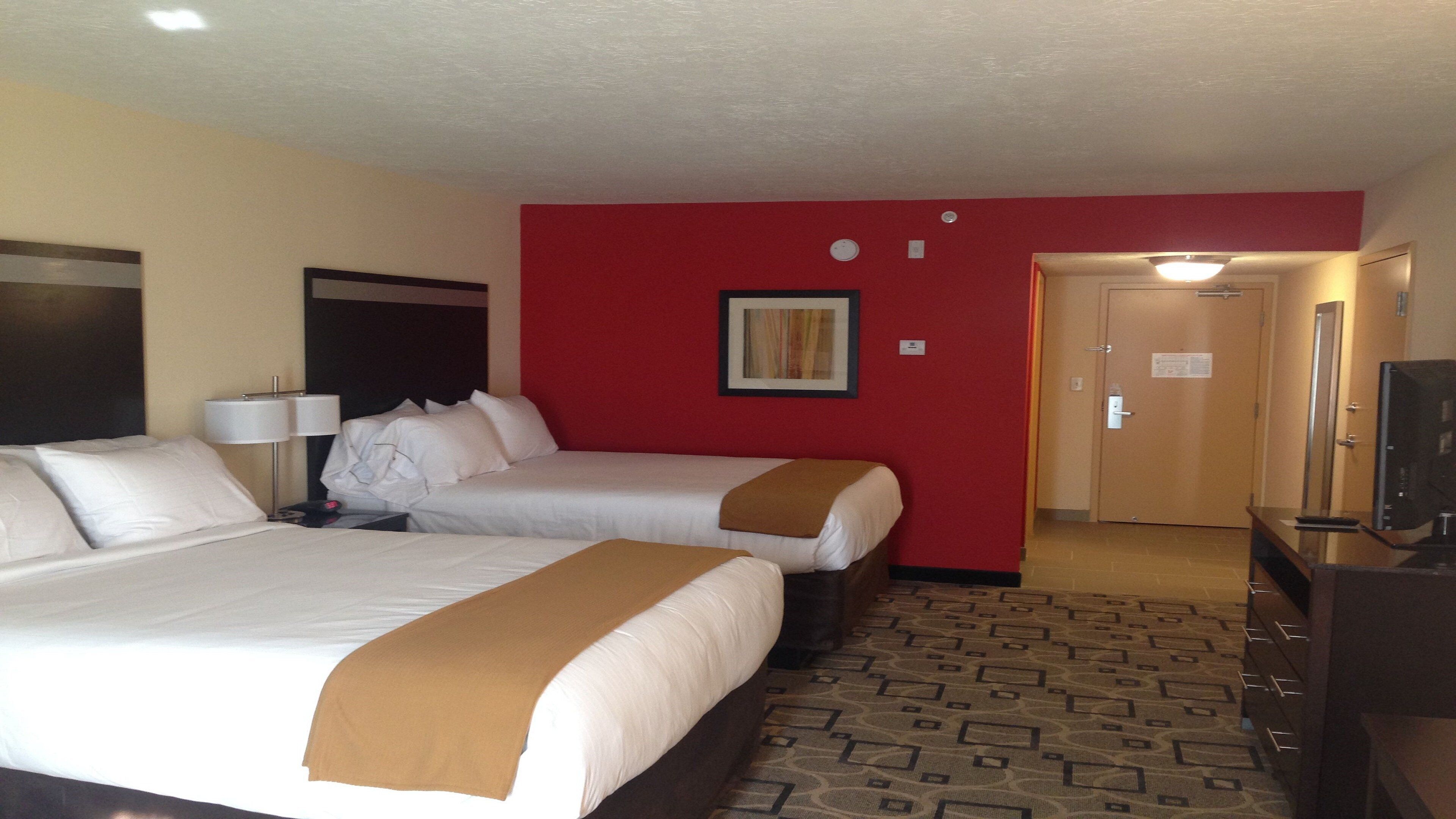 A hotel room with two beds, a television, a desk, and a red accent wall.