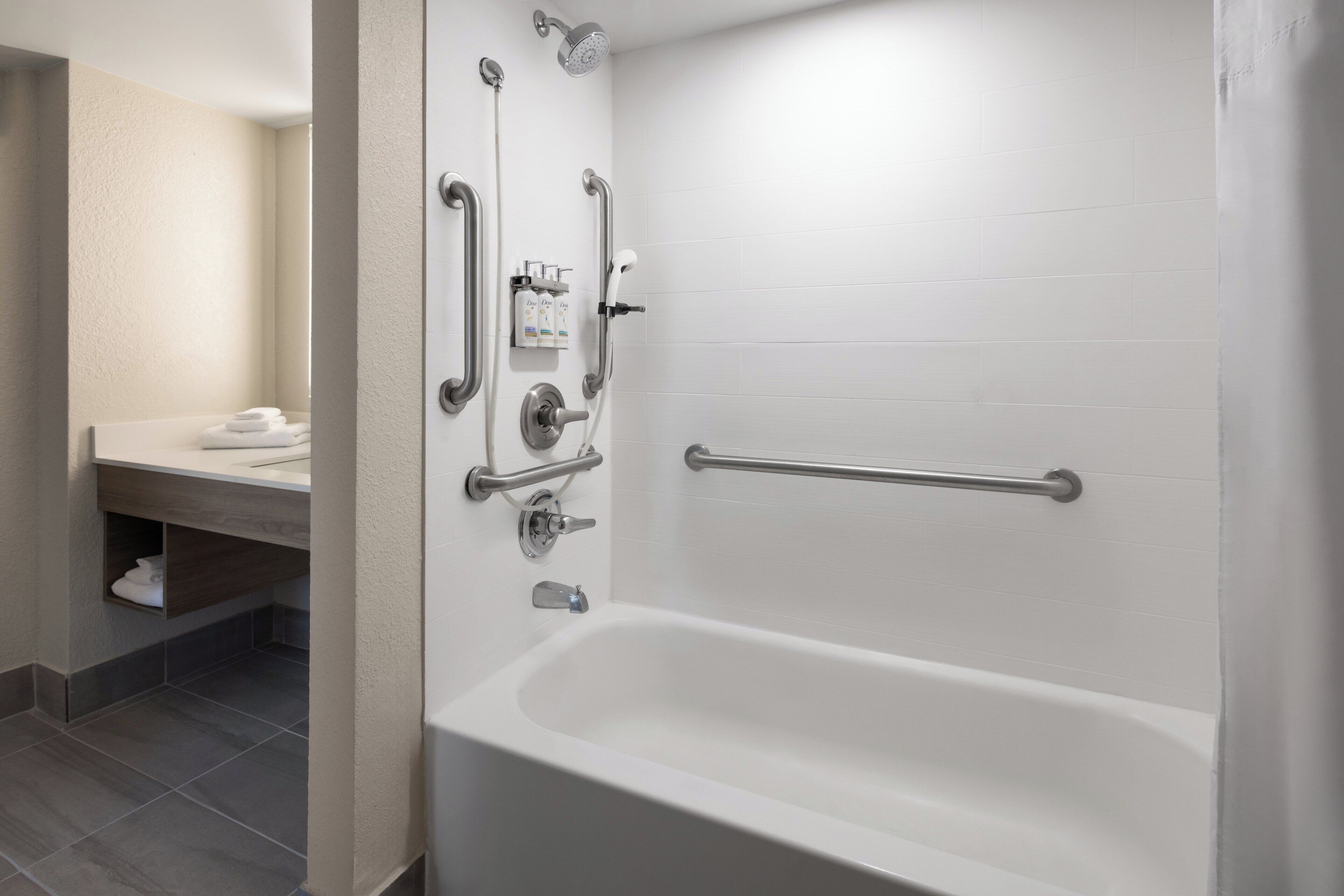 A modern bathroom with a white bathtub, grab bars, and a hand-held showerhead.