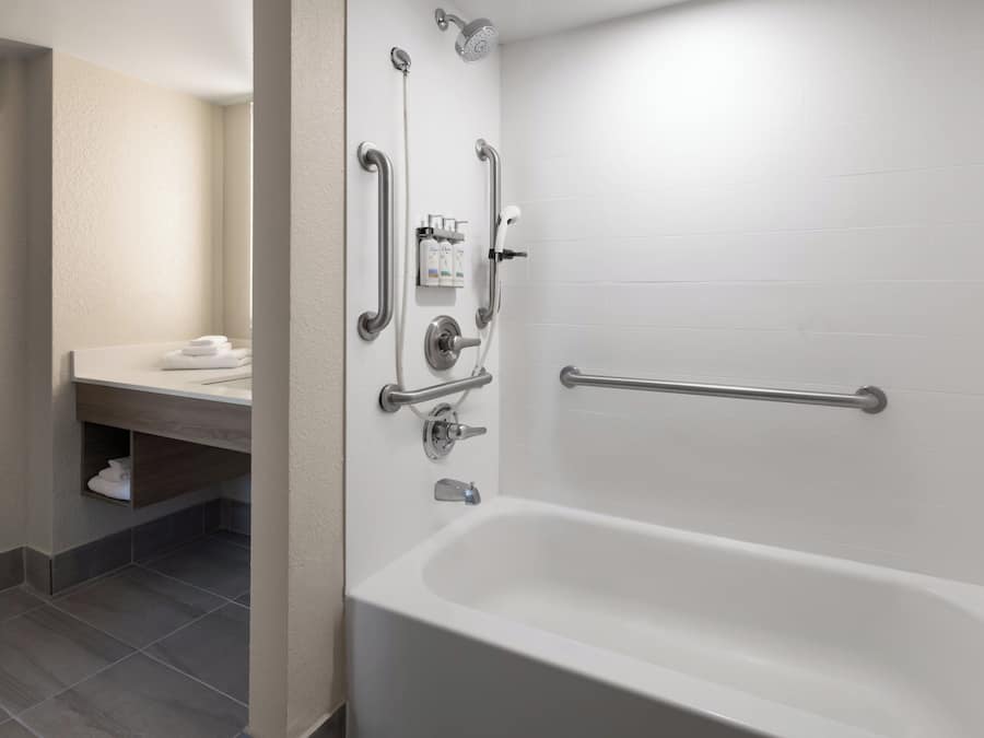 Een moderne badkamer met een wit bad, handgrepen en een douchehouder.