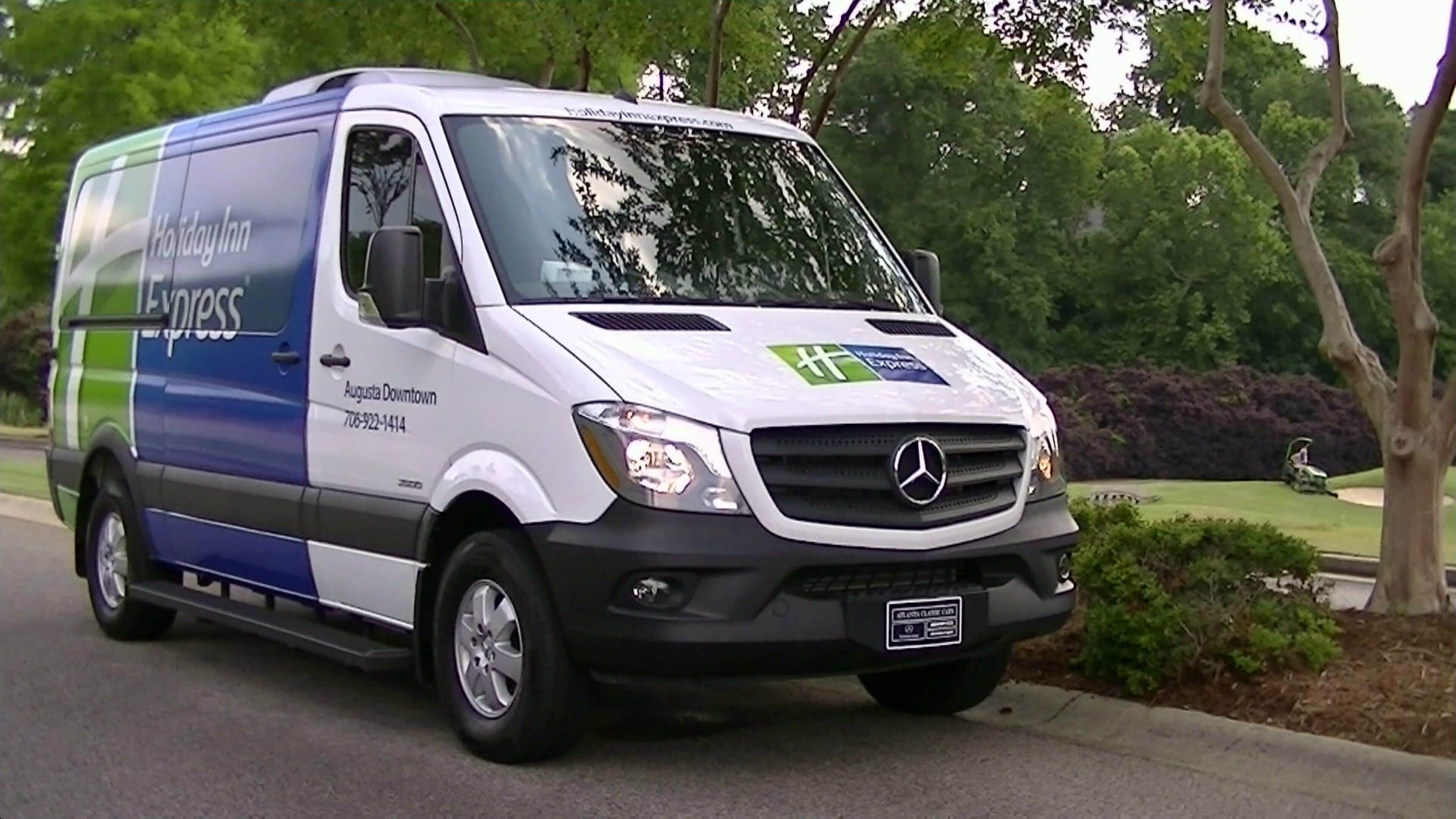 Ein weißer und blauer Lieferwagen mit 'Holiday Inn Express'-Branding steht auf einer Straße.