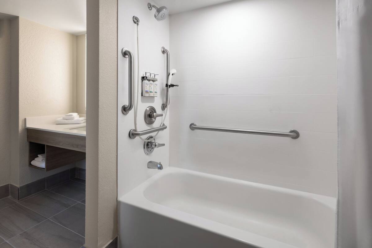A modern bathroom with a white bathtub, grab bars, and a hand-held showerhead.