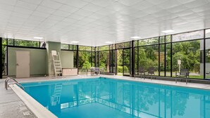 An indoor swimming pool with clear glass walls, a ladder, and a few chairs.