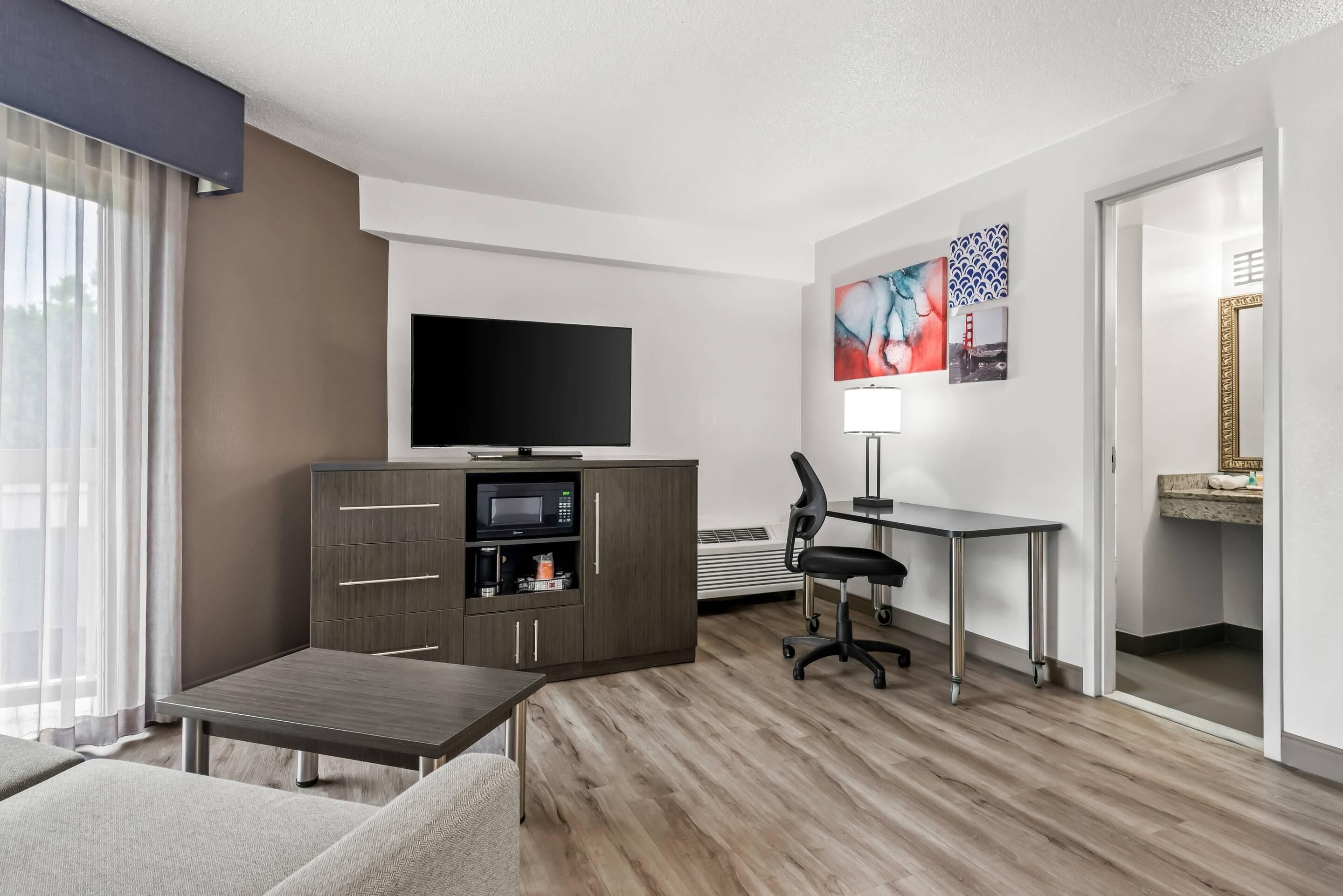 A modern hotel room with a flat-screen TV, a desk, a chair, a sofa, and a cabinet with a microwave.