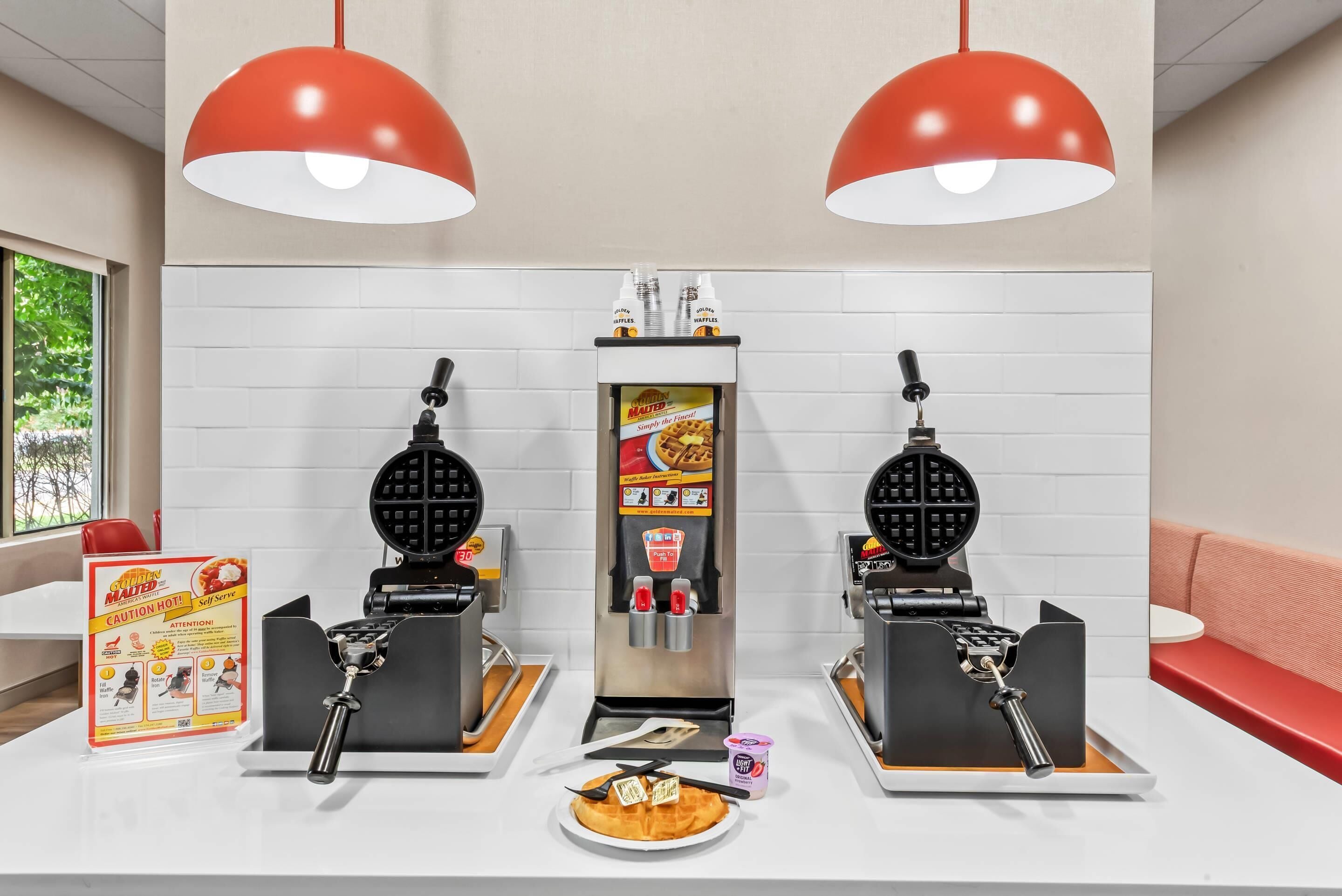 A self-service waffle station with two waffle makers, a waffle box, and a caution sign.