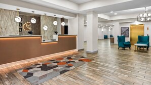 Un espace d’accueil d’hôtel avec un comptoir de réception en bois, des chaises de couleur turquoise et un tapis à motifs.
