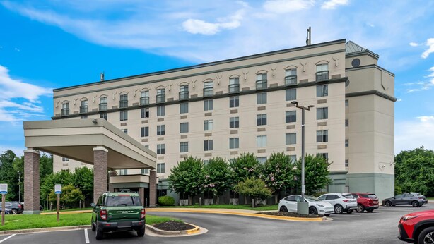 A multi-story hotel with a covered entrance, parking lot, and surrounding greenery.