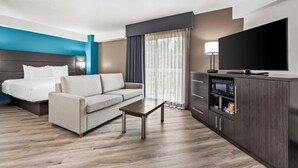 Une chambre d’hôtel moderne équipée d’un lit, d’un canapé, d’une table basse, d’une télévision et d’un mini-bar.