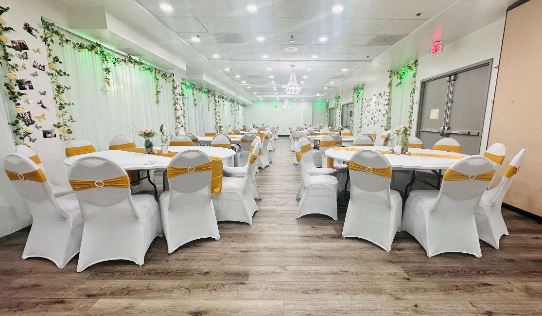 A banquet hall with white tables and chairs, each with a gold sashed chair.