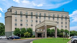 A multi-story hotel with a central entrance, parking area, and surrounding greenery.