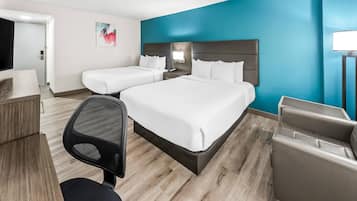 A hotel room with two beds, a desk, a chair, and a nightstand with a lamp.