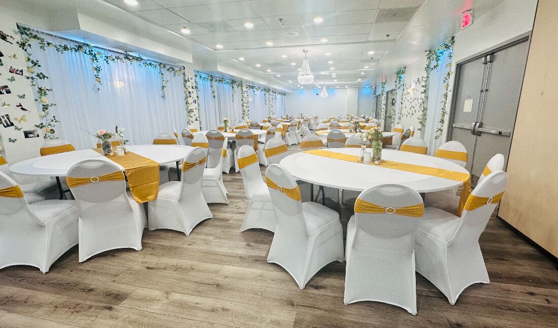 A banquet hall with round tables and white chairs, each with a gold sashed base.