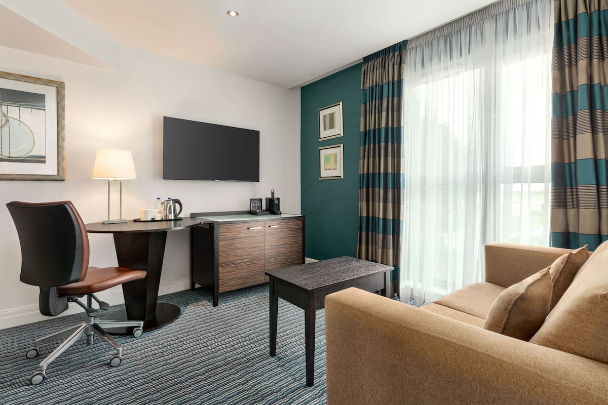 A hotel room with a desk, chair, sofa, and a flat-screen TV.